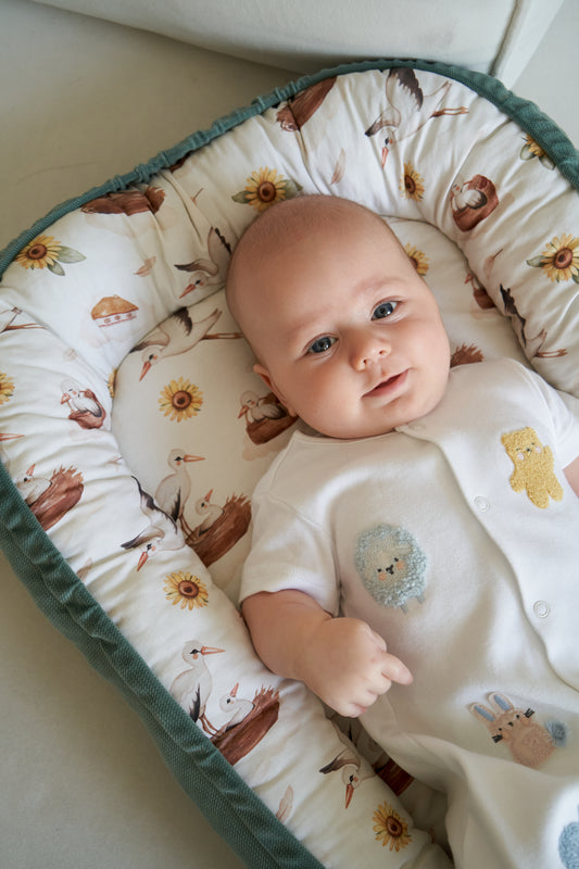 Baby cocoon from the My Ukraine collection with storks, sunflowers, and traditional Ukrainian elements on a light background