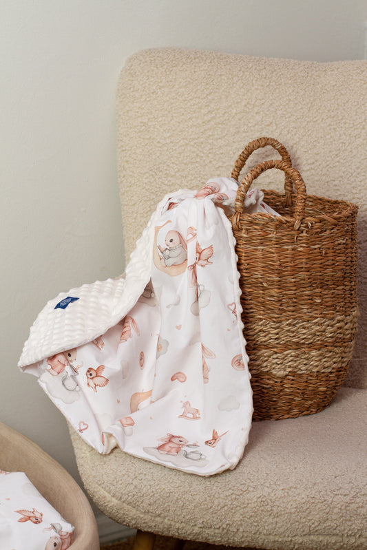 Folded baby blanket with Moony Dream print, made from Minky and cotton, showcasing bunnies and soft pastel clouds on a white surface.