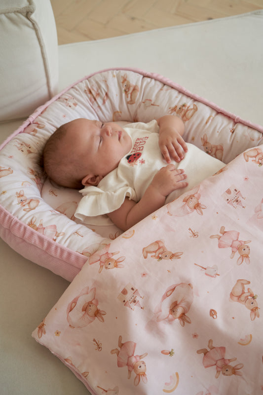 Baby cocoon from the Bunny Land collection with cute bunny illustrations in soft pink tones on a pale pink background