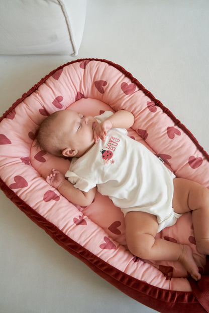 Baby sleeping peacefully in a cocoon with pink and red heart print, close-up view from above