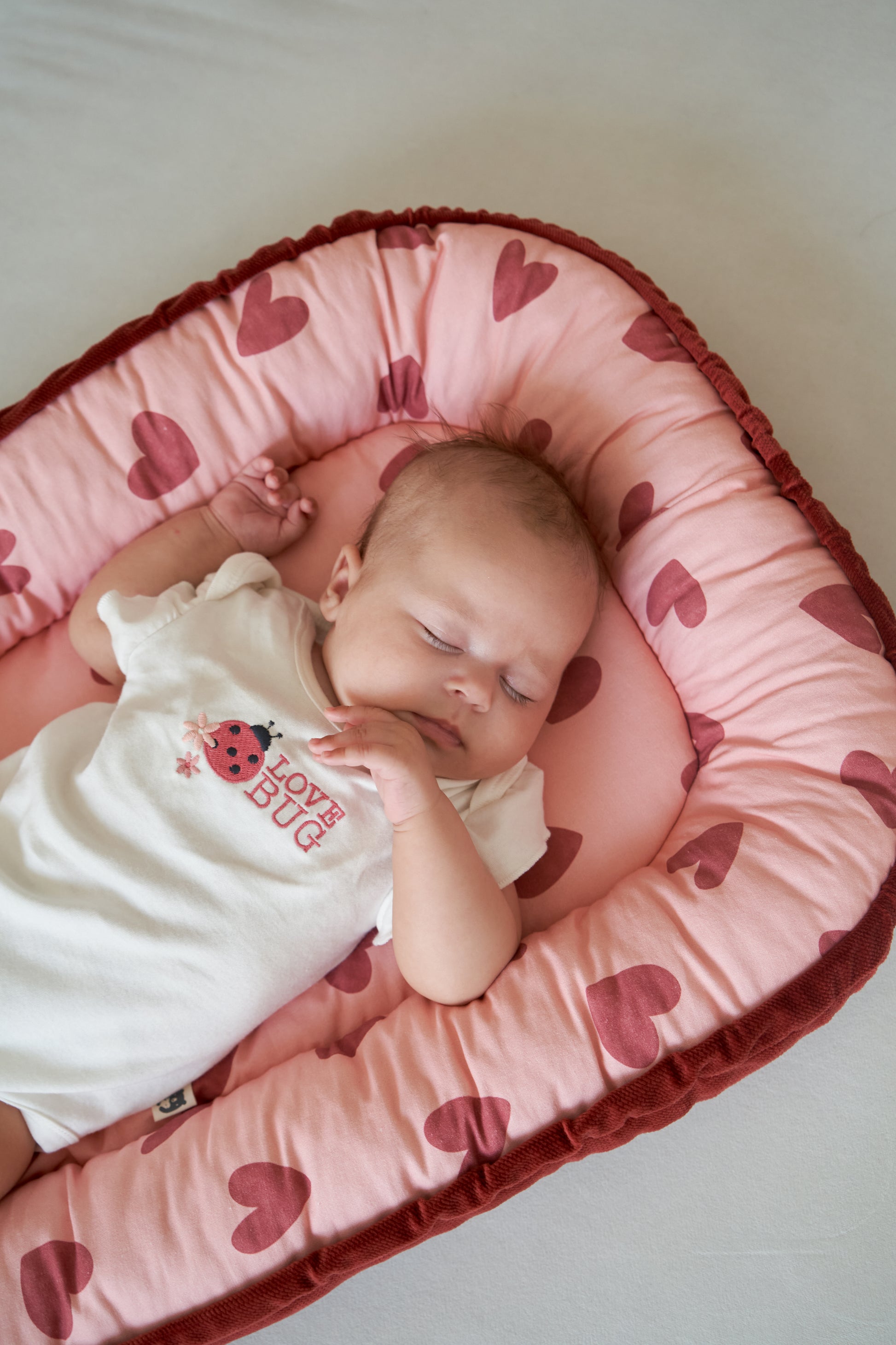 Newborn resting in a pink baby cocoon featuring a playful heart print, overhead perspective