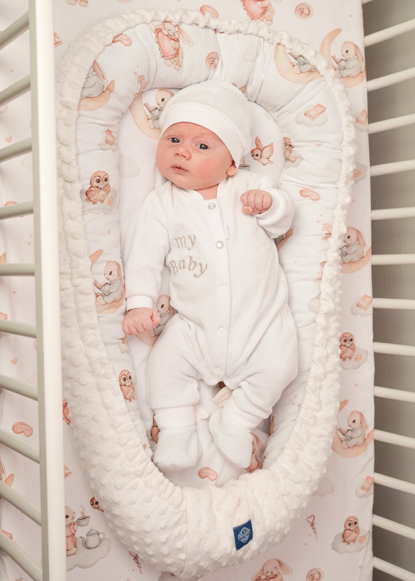 Newborn baby lying in a cozy cocoon for newborns, placed in a crib with soft bedding and playful animal patterns, ensuring comfort and safety