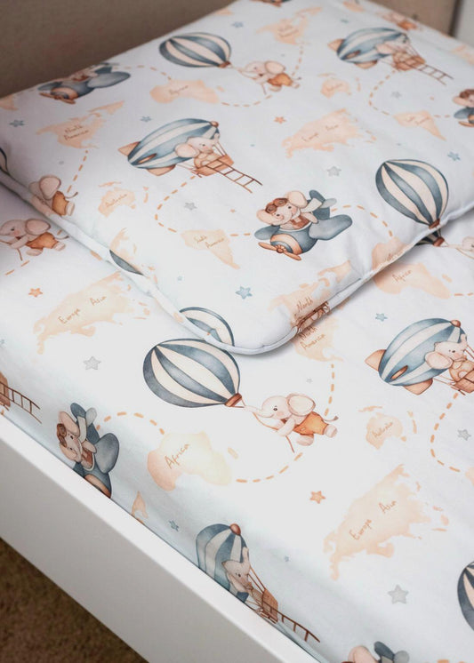 Baby pillow resting on matching bedding, featuring playful hot air balloon and airplane patterns, designed for comfort and a cohesive crib decor in a light blue theme