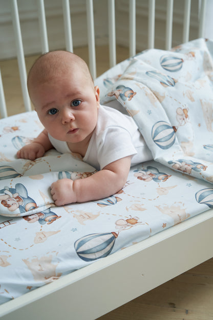 Baby lying on a bed with hot air balloon-themed bedding in pastel colors