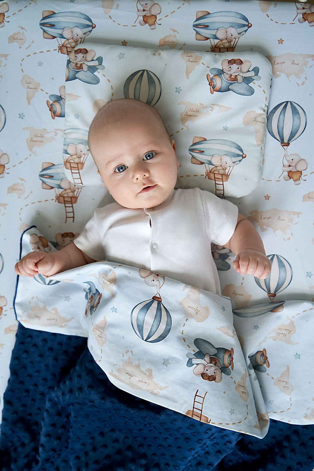 Top view of baby lying on soft baby bedding with aviation print, featuring a matching pillow and minky blanket