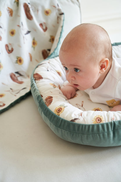 Baby practicing tummy time in a MyUkraine baby cocoon, showcasing stork and sunflower patterns, side view