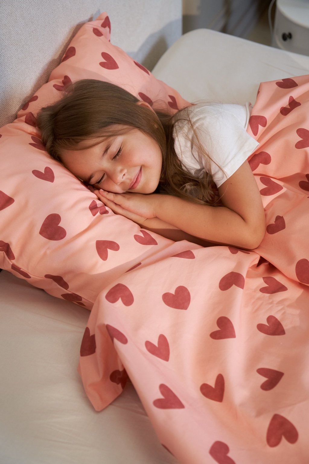 A girl peacefully sleeping on the Heartland pink bedding set with a heart pattern, featuring soft and cozy fabric