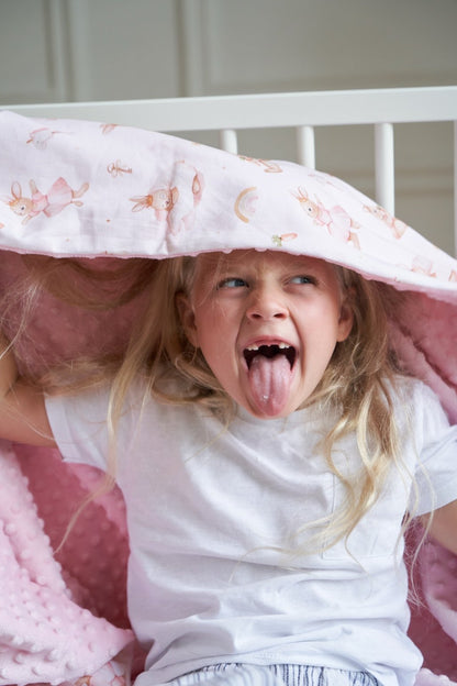 Child playing under a pink Bunny Land blanket with rabbit print