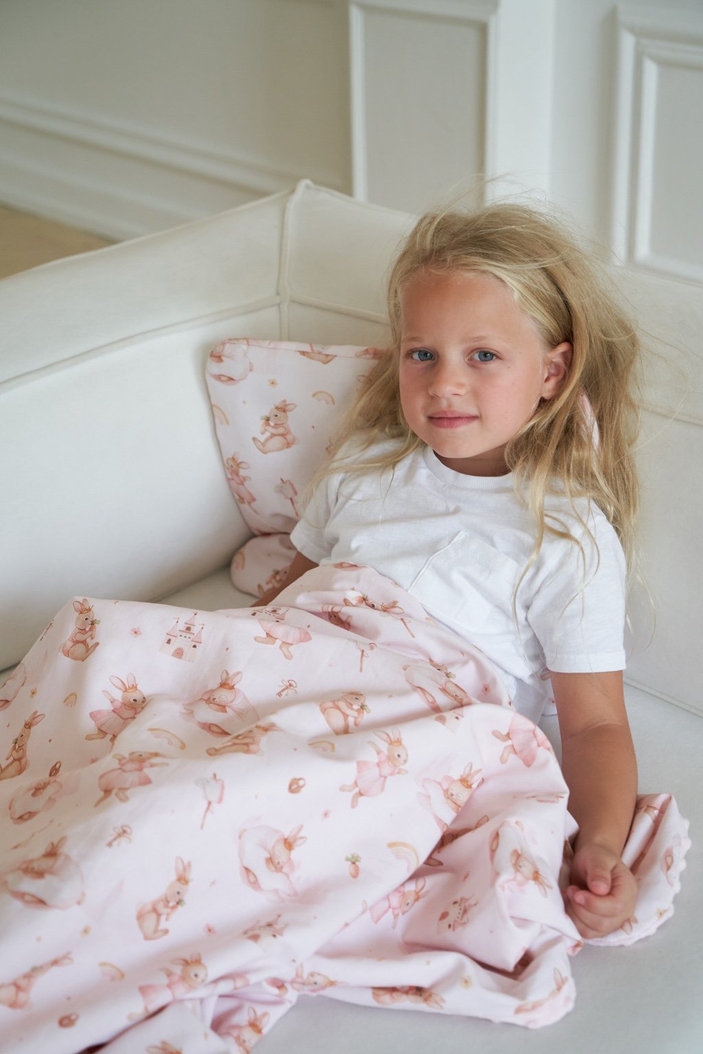 Young child sitting on a couch with a children’s orthopedic pillow and soft baby bedding, featuring playful bunny-themed patterns