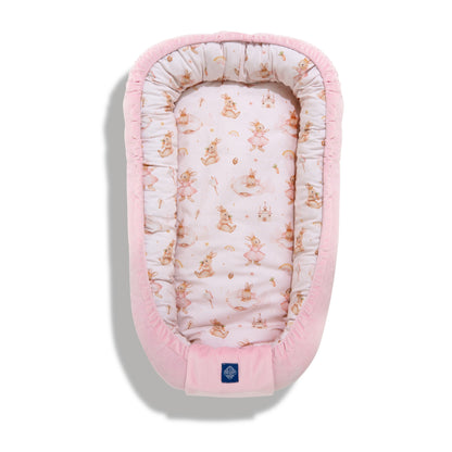 Baby cocoon from the Bunny Land collection with cute bunny illustrations in soft pink tones on a pale pink background