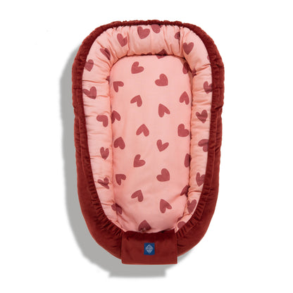 Baby cocoon from the Hearts Red collection with a red heart pattern on a light pink background